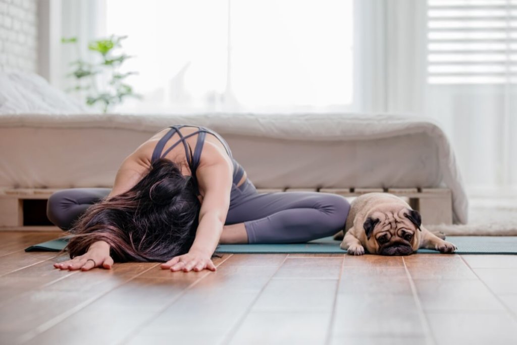 Puppy Yoga – kobieta i Mops relaksujący się podczas ćwiczeń na macie w domowym zaciszu.